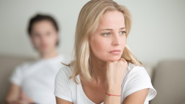 Serious sad woman thinking over a problem, man sitting aside, end of long-term relations, an alcoholic, drug addicted partner, poor conflict management skill, ongoing disagreements with adult son