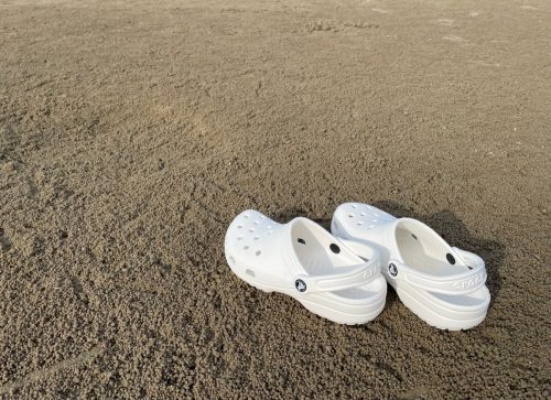 A pair of white Crocs footwear on a sandy beach