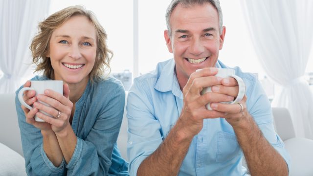 Smiling,Middle,Aged,Couple,Sitting,On,The,Couch,Having,Coffee