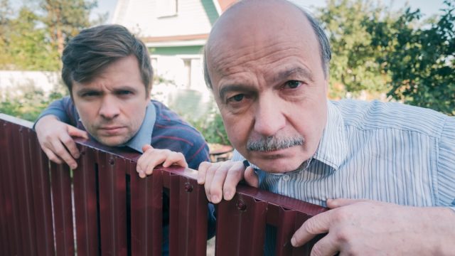 two angry caucasian men carefully watching over the fence. Concept of curious neighbors and private life