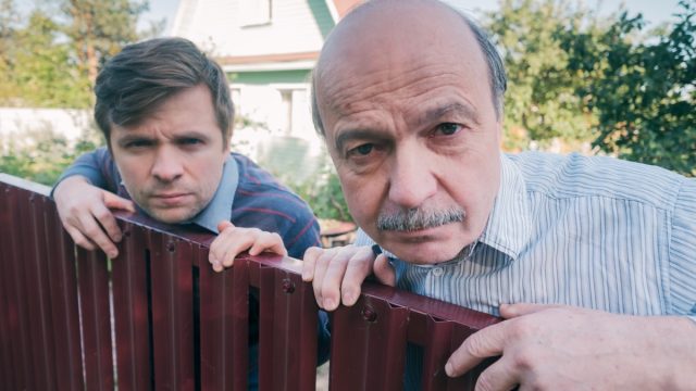 two angry caucasian men carefully watching over the fence. Concept of curious neighbors and private life