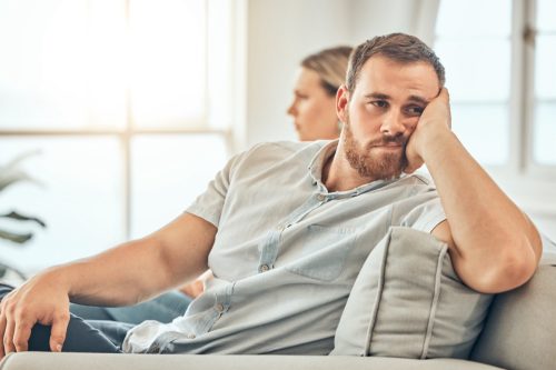 Young caucasian man with a beard looking unhappy and annoyed while sitting on the couch during an argument with his wife at home. Bored man sitting and thinking on the couch.