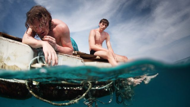 Two men floating in a sea with sad faces