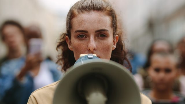 Female,Activist,Protesting,With,Megaphone,During,A,Strike,With,Group