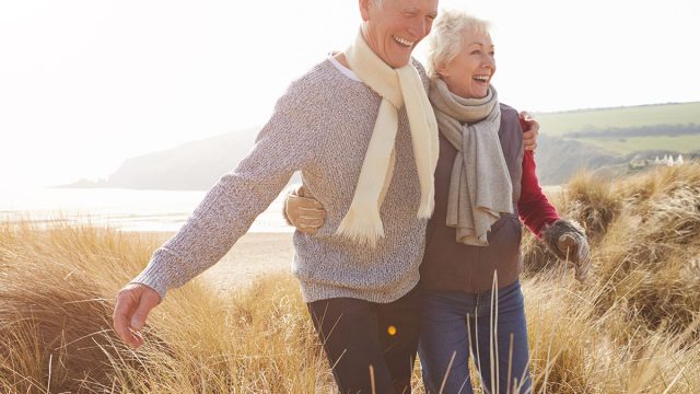 Senior,Couple,Walking,Through,Sand,Dunes,On,Winter,Beach