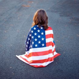 Sad lonely woman sitting down with the american flag wrapped around her.