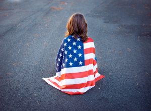 Sad lonely woman sitting down with the american flag wrapped around her.