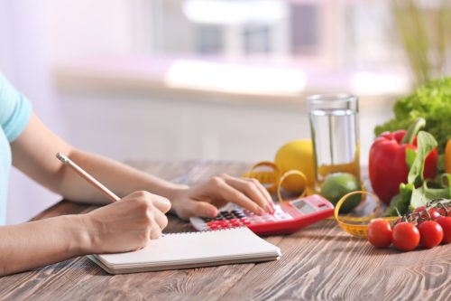 Young woman calculating calories at table.