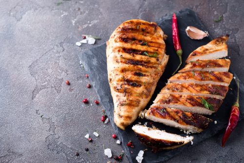 whole and sliced chicken breast with spices on a stone board, top view copy space