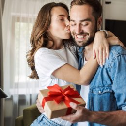 Young couple at home, celebrating with a gift box exchange, kissing