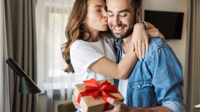 Young couple at home, celebrating with a gift box exchange, kissing