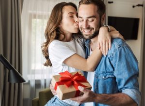 Young couple at home, celebrating with a gift box exchange, kissing