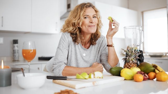 Portrait, fruit salad and apple with a senior woman in the kitchen