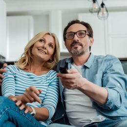 Smiling mature couple watching tv on sofa.