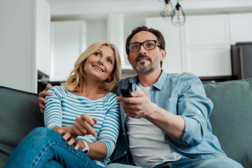 Smiling mature couple watching tv on sofa.