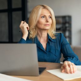 Serious pensive mature businesswoman with computer making notes.