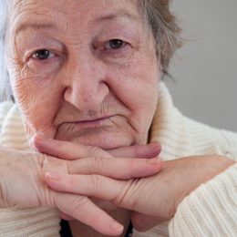 Elderly woman with beautiful wrinkled face is holding pills in her hands to choose medicines. Selective focus depth of field