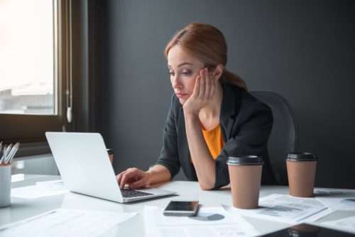 Portrait of serious weary businesswoman typing in laptop while sitting at table in apartment