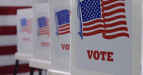 Straight on row of voting booths at polling station during American election. US flag in background.