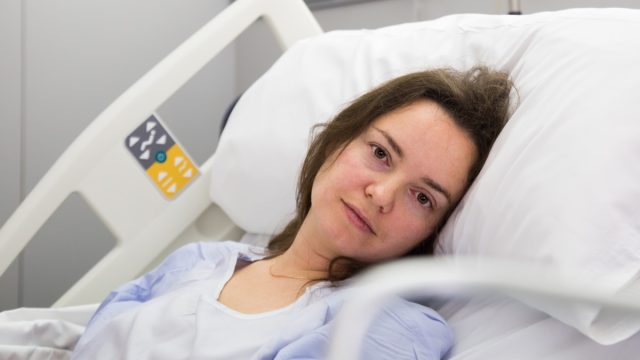 Brunette adult woman is lying fever on the bed in hospital indoor