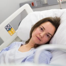 Brunette adult woman is lying fever on the bed in hospital indoor