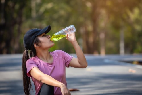 Asian woman athlete is drinking water with electrolytes after exercise.