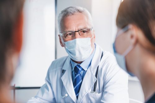 Mature doctor in protective mask during meeting in conference room.