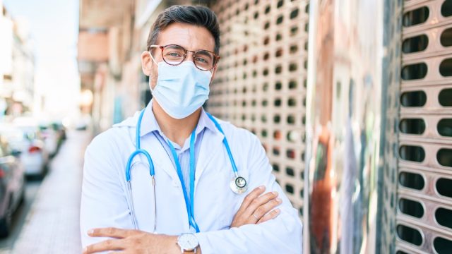 Doctor wearing uniform and coronavirus protection medical mask standing at town street.