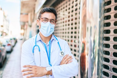 Doctor wearing uniform and coronavirus protection medical mask standing at town street.