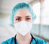 Young female doctor in a green uniform with surgical cap and protection mask, close up portrait, horizontal background. Prevention of Covid-19.