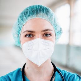 Young female doctor in a green uniform with surgical cap and protection mask, close up portrait, horizontal background. Prevention of Covid-19.