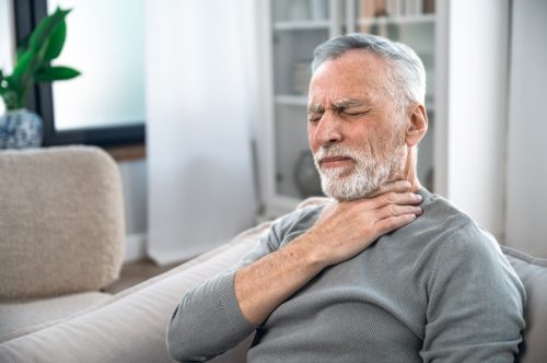 Mature aged man suffering from strong throat sore or angina.