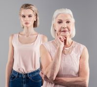Contemplative senior lady touching her chin while thinking out while her daughter suspect nothing