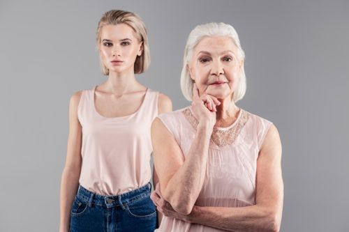 Contemplative senior lady touching her chin while thinking out while her daughter suspect nothing