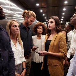 Work colleagues stand waiting together in an elevator at their office.
