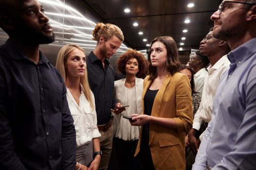 Work colleagues stand waiting together in an elevator at their office.