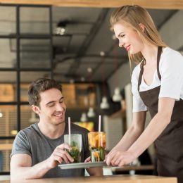 Smiling waitress in apron bringing order to client in cafe.