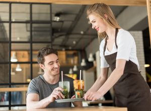 Smiling waitress in apron bringing order to client in cafe.