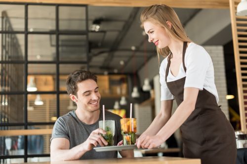 Smiling waitress in apron bringing order to client in cafe.