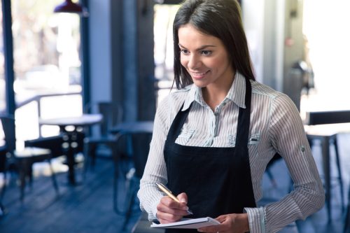Smiling female waiter in apron with notepad and pen in cafe.