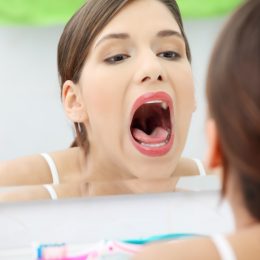 Woman stands about a mirror in a bathroom with open mouth.