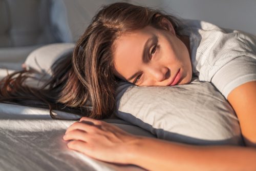 Tired woman lying on pillow in bed.