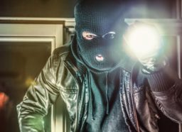 Masked burglar with torch and crowbar breaking and entering into a house - shot with dramatic motion