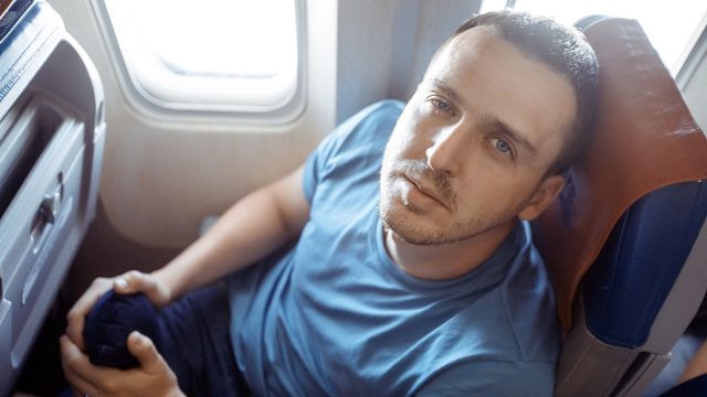 Male passenger feeling dizzy having airsickness while traveling on plane. Man looking at camera