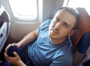 Male passenger feeling dizzy having airsickness while traveling on plane. Man looking at camera
