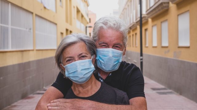 couple of two seniors wearing medical mask to prevent coronavirus (covid-19) or another type of virus - close up of faces in middle of street - protect happy cheerful people looking at the camera fun
