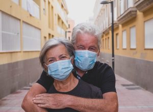 couple of two seniors wearing medical mask to prevent coronavirus (covid-19) or another type of virus - close up of faces in middle of street - protect happy cheerful people looking at the camera fun