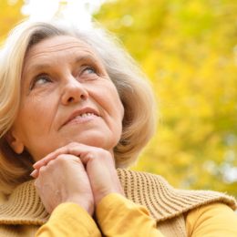 Older woman stands on a background of yellow autumn.