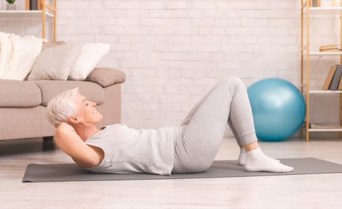 Senior woman doing abs exercise on floor at home.