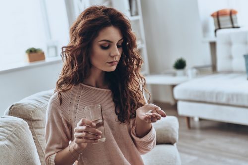 Young woman holds pills at her hand.